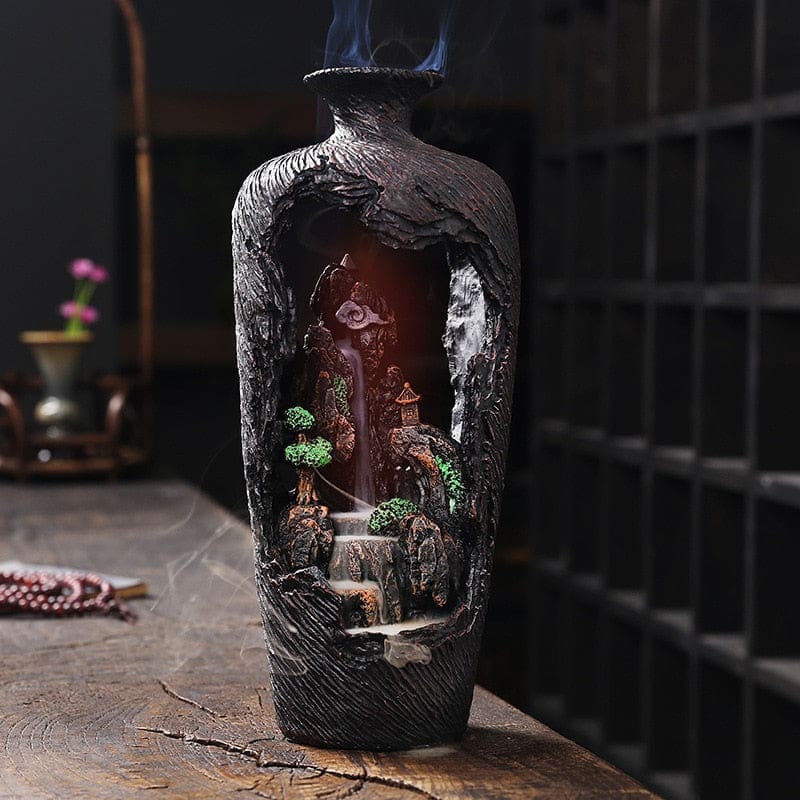 Full red-lit view of the brown vase-shaped incense burner, with light glowing through the open miniature landscape.