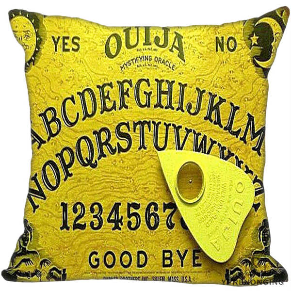 Bright yellow square Ouija cushion cover with dark board lettering, decorative corner illustrations and an angled yellow planchette printed over the alphabet.